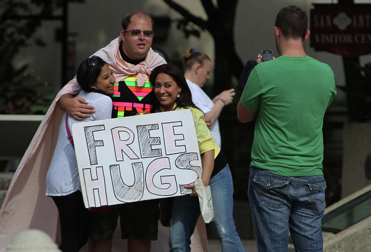 Christopher Webster hugs Laura Reyna (left) and Denise Gongora while their friend Mike Simmons takes their picture near Alamo Plaza this month. Webster offers free hugs there most Saturday mornings.