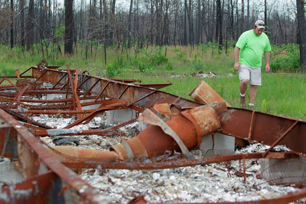 Mike Costello, a volunteer for the Waller County Long-term Recovery Committee and Northeast Texas Conference of The Methodist Church, walks around a wildfire damaged and abandoned property in the Remington Forest West subdivision, Wednesday, May 9, 2012 in Magnolia, TX. The neighborhood is slowly recovering after being heavily damaged by wildfires last year.
