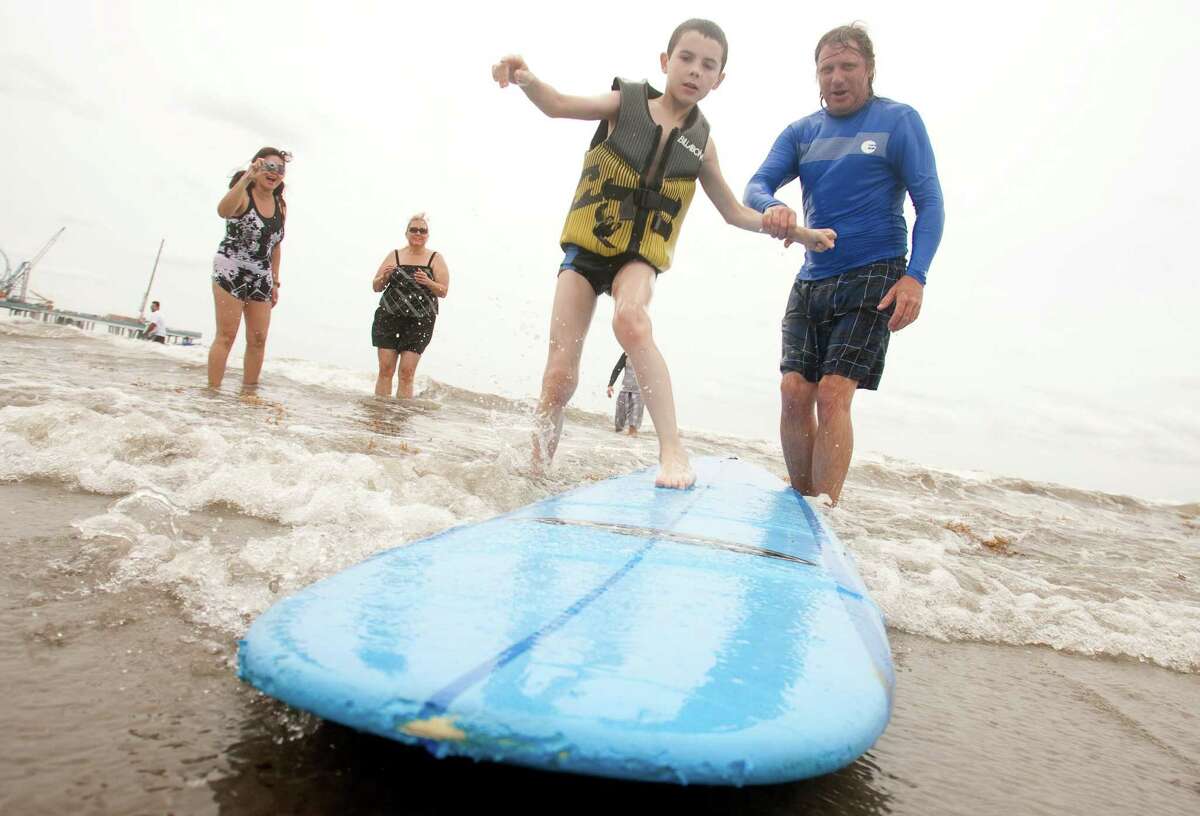 Volunteer Danny Clements helps Jose Rueda, 11, climb onto the surfboard during the Waves of Impact free surf camp for children with autism.