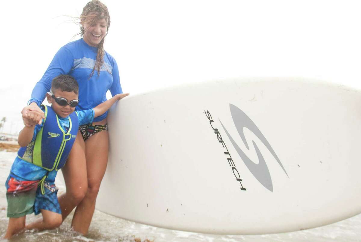 Volunteer Andi Fogel helps Apollo Contreras, 5, into the water during the Waves of Impact free surf camp for children with autism at Seawall Blvd.