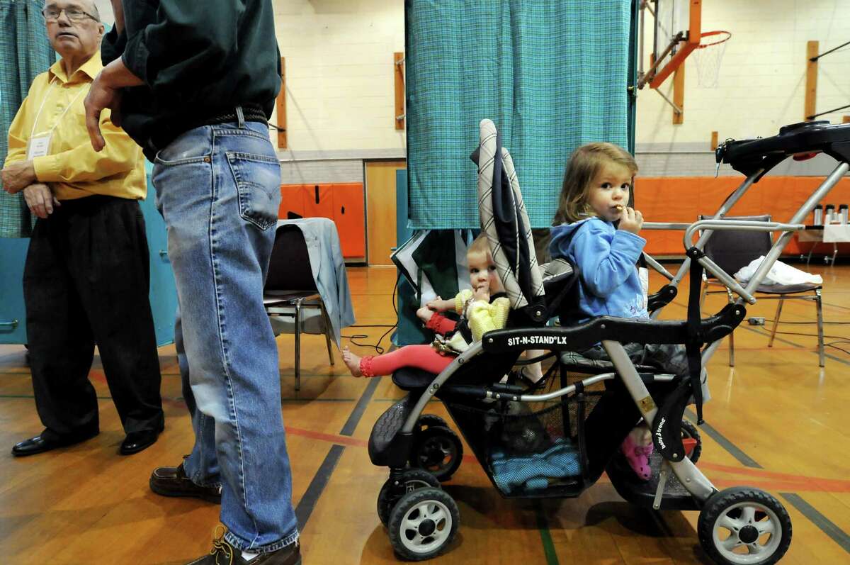 Ruthie McAvoy, 10 months, center, and her sister, Margot, 2, right, wait for their mother, Rose, to vote on the school budget on Tuesday, May 15, 2012, at Bethlehem High in Bethlehem, N.Y. At left is election inspector Neil Brown. (Cindy Schultz / Times Union)