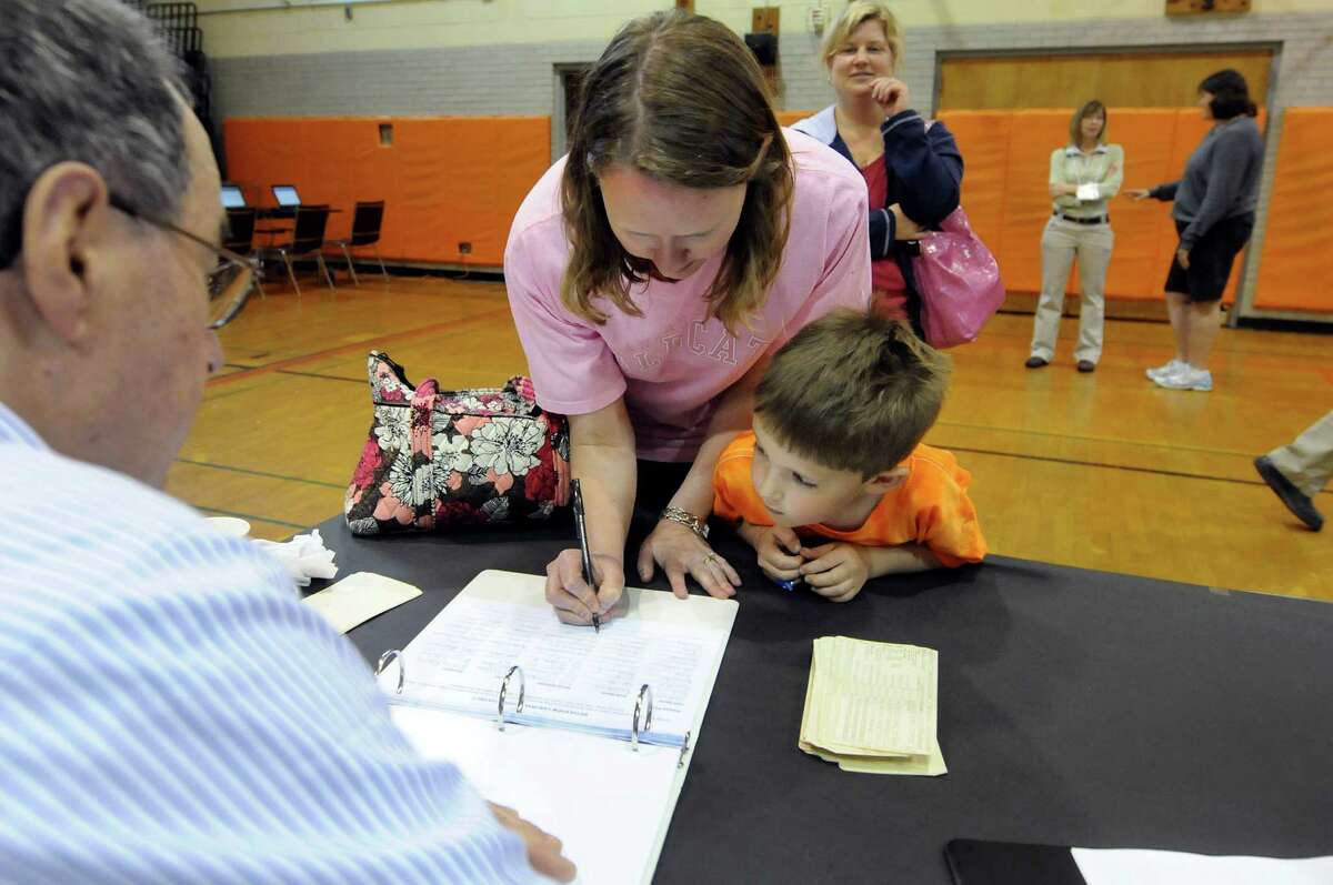 Grant Rinckey, 5, center, stays close as his mother, Tara, signs in to vote on the school budget on Tuesday, May 15, 2012, at Bethlehem High in Bethlehem, N.Y. At left is election inspector Warren Stoker. (Cindy Schultz / Times Union)