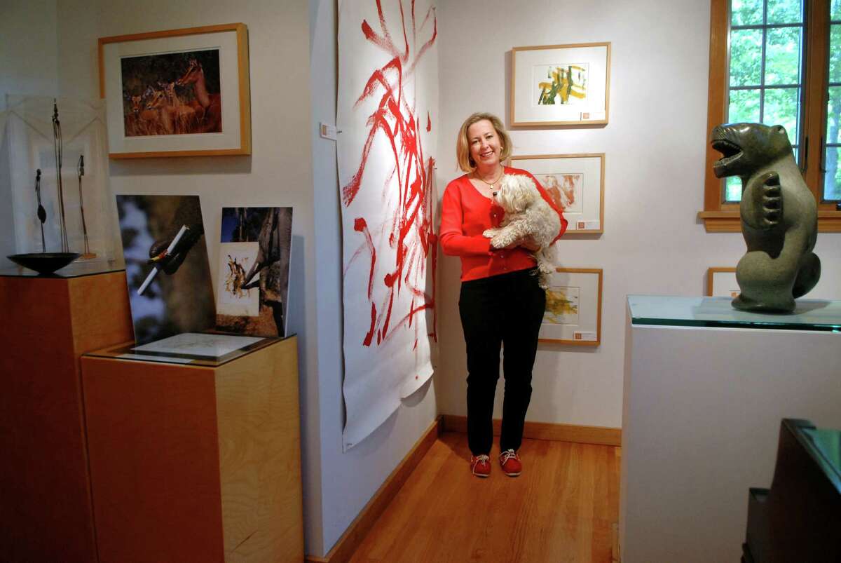 Elizabeth Ball, the CEO of TFI Envision, holds her dog "Honey" in her gallery, the Pierce-Ball Gallery in Stamford, Conn. on Saturday May 12, 2012 surronded by paintings done by elephants.