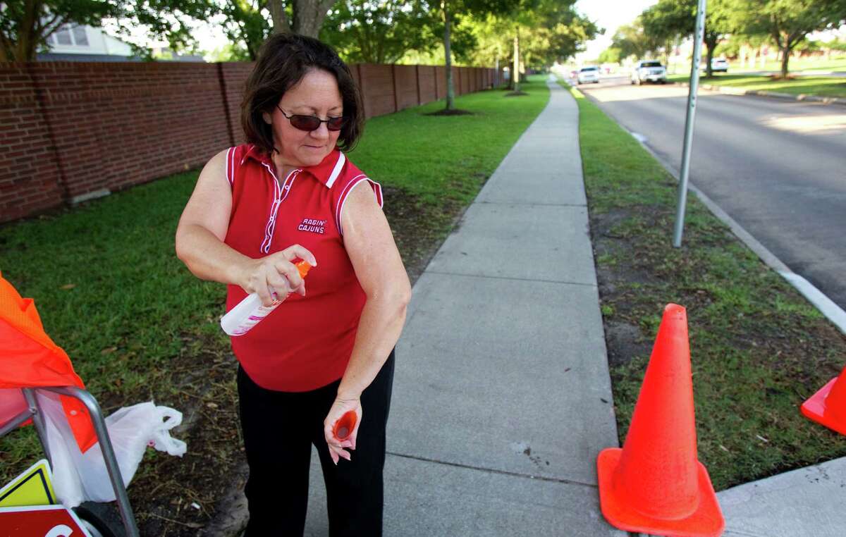 School crossing guard Angie Foret sprays her arms before her shift Wednesday in Pearland. Foret said mosquitoes have been a real problem at her crossing.
