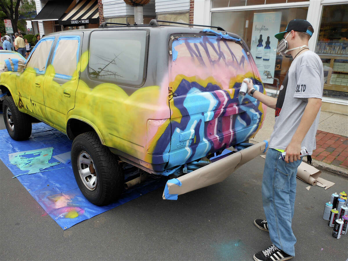 Austin Brodsky, an artist and clothes designer, graffiti tags a 4Runner at the Art About Town fest on Thursday evening in downtown Westport.