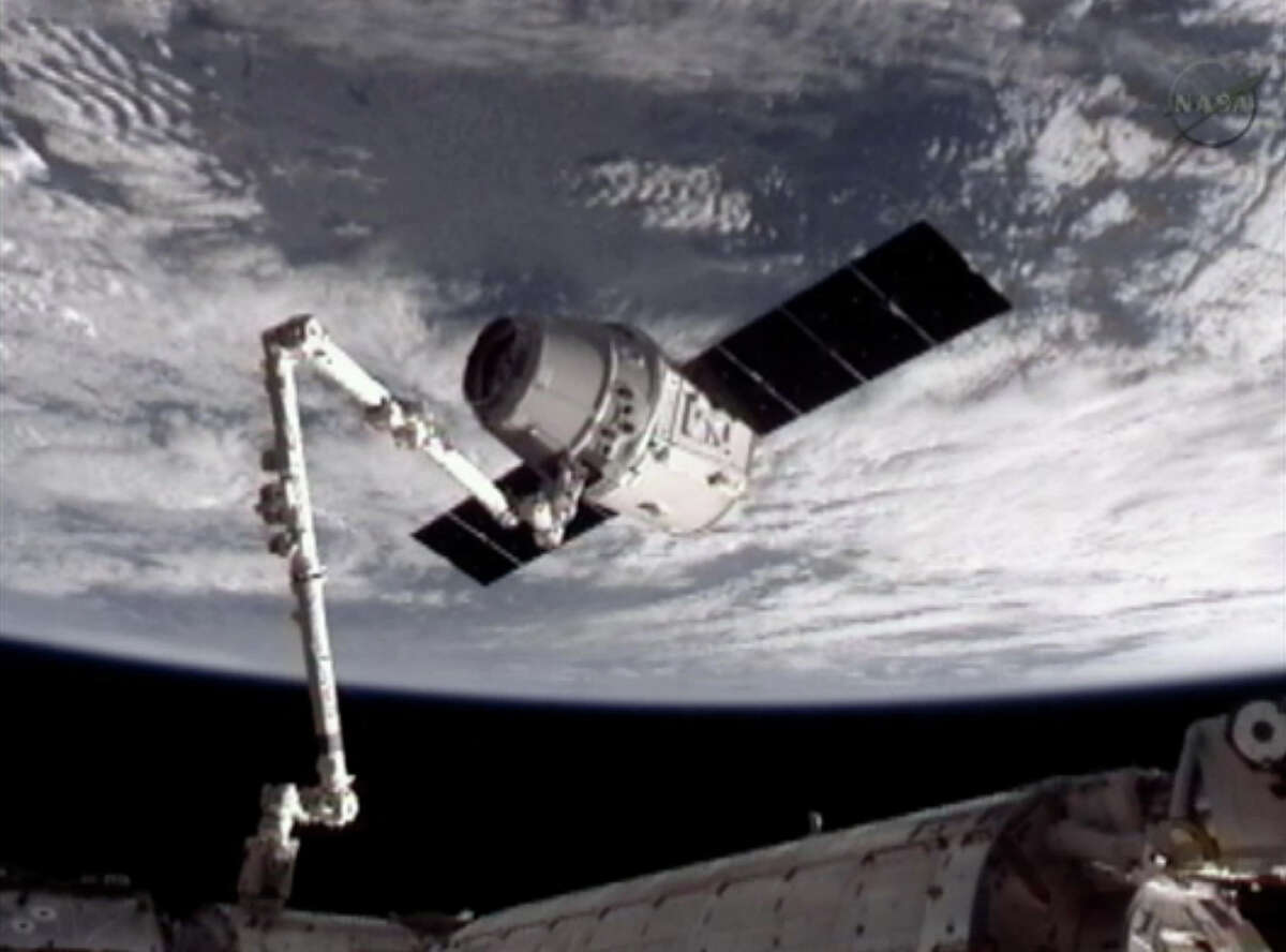 This image provided by NASA-TV shows the SpaceX Dragon commercial cargo craft, top, after Dragon was grappled by the Canadarm2 robotic arm and connected to the International Space Station, Friday, May 25, 2012. Dragon is scheduled to spend about a week docked with the station before returning to Earth on May 31 for retrieval.