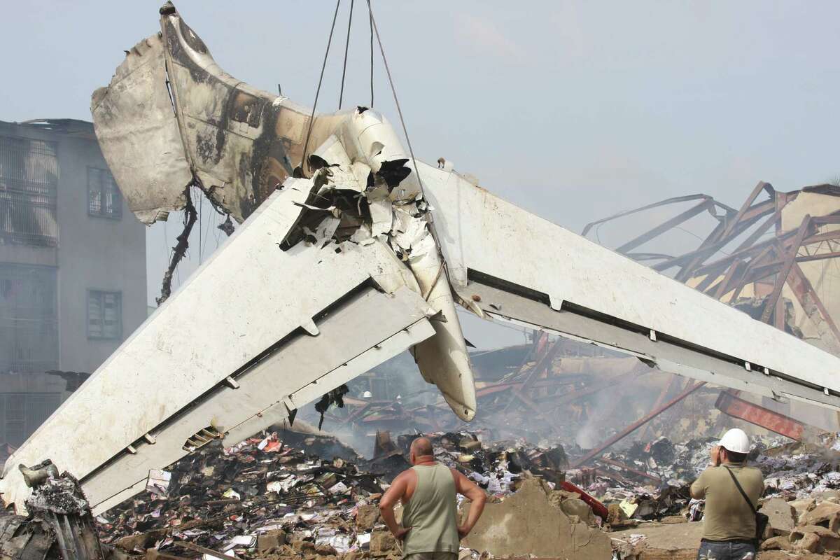 Workers watch as the tail of a crashed commercial airplane is lifted by a crane in Lagos, Nigeria, Monday, June 4, 2012. Emergency workers in Nigeria used cadaver dogs and cranes to search for corpses Monday at the site where an American-built airliner plunged to earth, killing all 153 aboard. Rescue officials said they fear many more people may have perished on the ground in the crash Sunday. (AP Photo/Jon Gambrell)