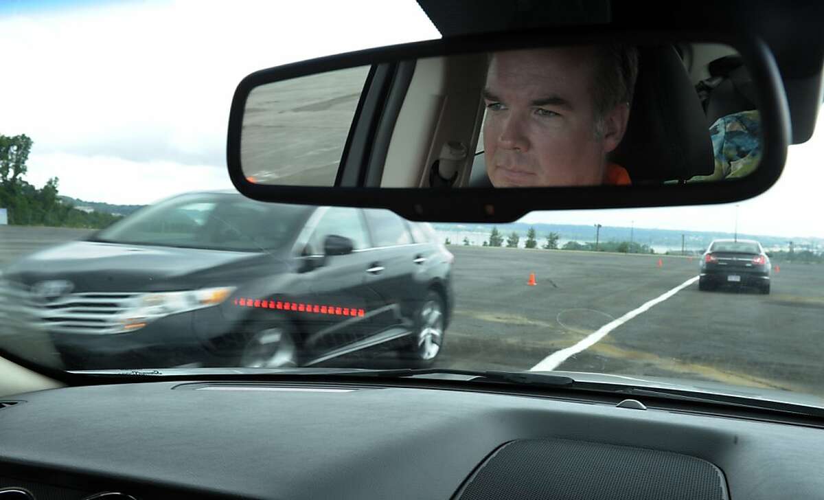 In this photo taken, Tuesday, May 22, 2012, professional test driver J.D. Ellis of Cincinnati, Ohio, demonstrates the dashboard warning signal in a Ford Taurus, at an automobile testing area in Oxon Hill, Md. The display at a recent transportation conference was a peek into the future of automotive safety: cars that to talk to each other and warn drivers of impending collisions. Later this summer, the government is launching a yearlong, real-world test involving nearly 3,000 cars, trucks and buses using volunteer drivers in Ann Arbor, Mich. (AP Photo/Susan Walsh)
