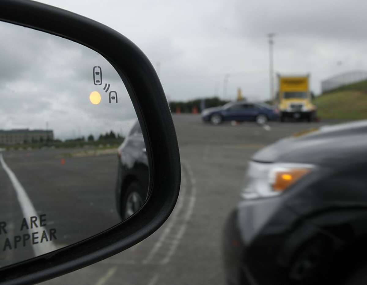 In this photo taken, Tuesday, May 22, 2012, professional test driver J.D. Ellis of Cincinnati, Ohio, demonstrates the side mirror warning signal in a Ford Taurus at an automobile testing area in Oxon Hill, Md. The display at a recent transportation conference was a peek into the future of automotive safety: cars that to talk to each other and warn drivers of impending collisions. Later this summer, the government is launching a yearlong, real-world test involving nearly 3,000 cars, trucks and buses using volunteer drivers in Ann Arbor, Mich. (AP Photo/Susan Walsh)