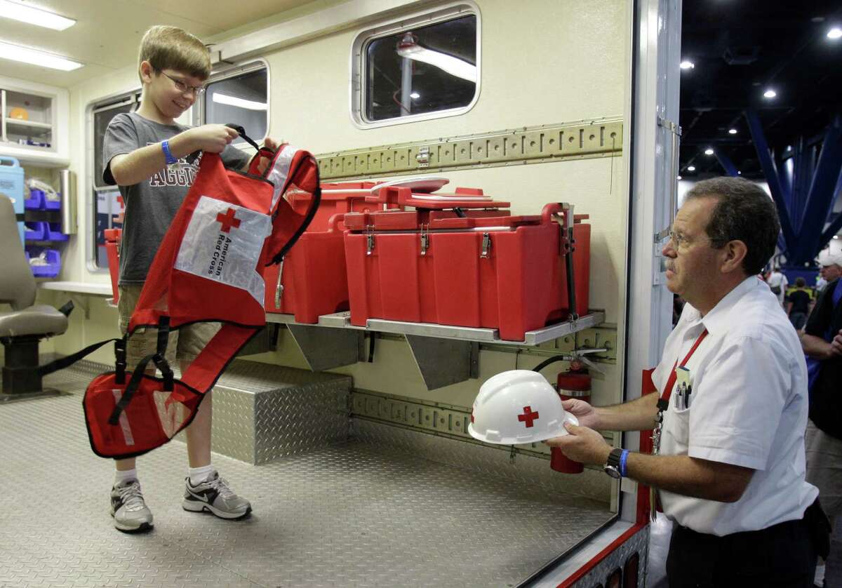 Ryan Williamson, 10, of El Campo is helped by Red Cross volunteer, Mark Zentner, of Houston, to try on a vest and hard hat inside a Red Cross emergency response vehicle during the Houston/Galveston National Weather Service 2012 Hurricane Workshop at the George R Brown Convention Center.