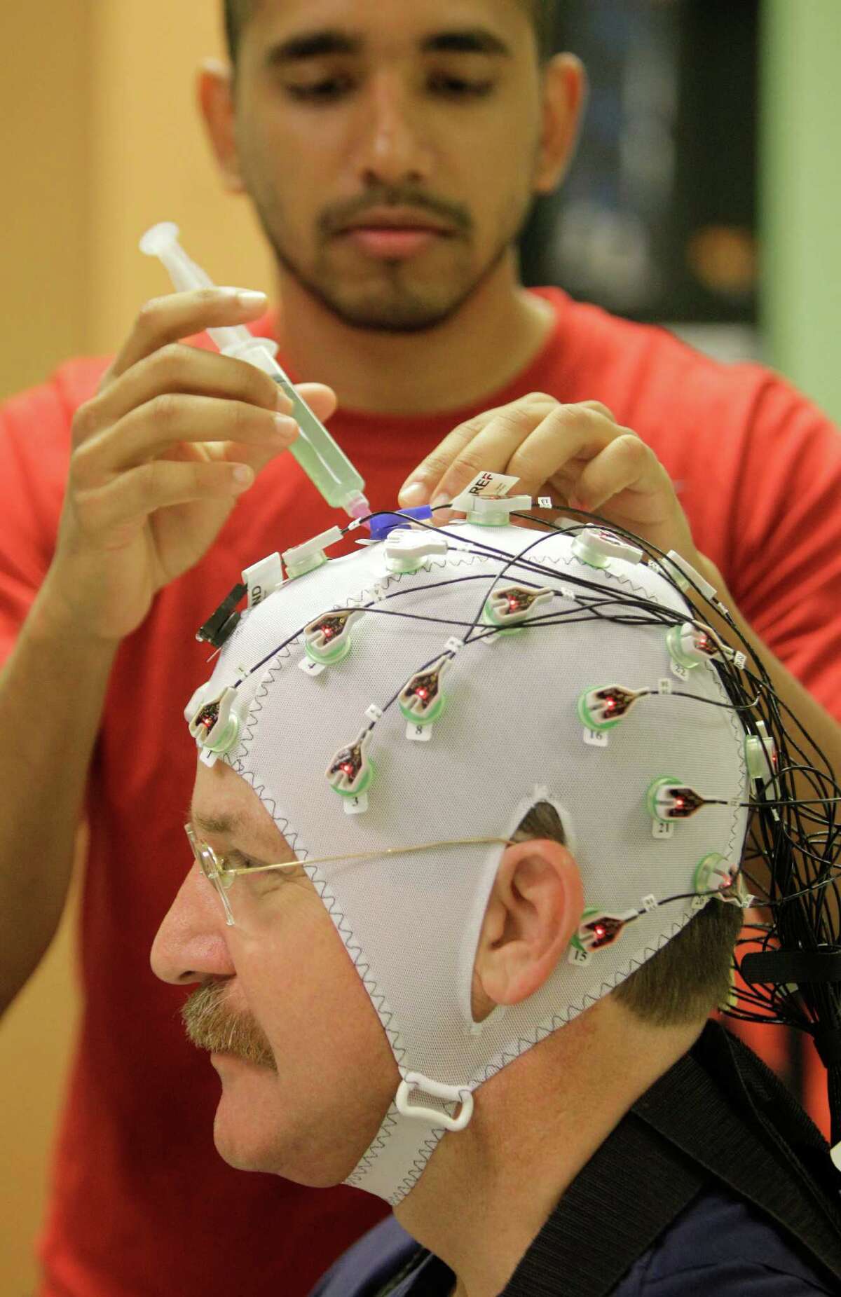 University of Houston graduate student, Harsha Agashe, applies conducting gel to the skullcap of electrodes to Dr. Eugene Alford, right, for his testing of a robotic exoskeleton.