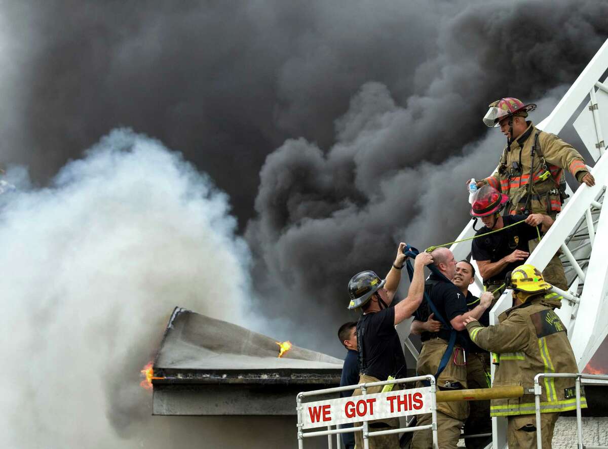 Houston firefighters help a fellow firefighter, who suffered heat exhaustion, off a ladder as they battle a multiple alarm blaze at a warehouse which stores oil spill clean-up products Thursday, June 14, 2012, in Houston. One firefighter was treated at the scene for heat exhaustion.