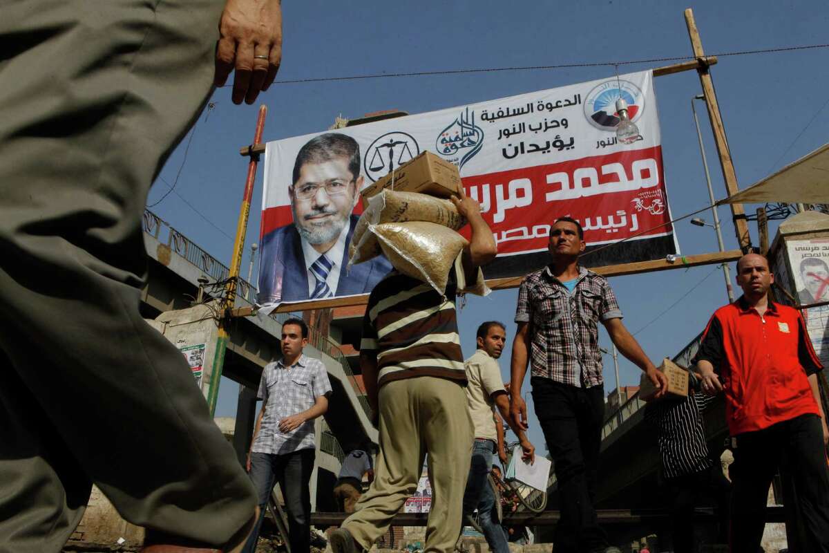 Egyptians walk under a billboard supporting presidential candidate Mohammed Morsi in Zagazig, 63 miles (100 kilometers) northeast of Cairo, Egypt, Saturday, June 16, 2012.