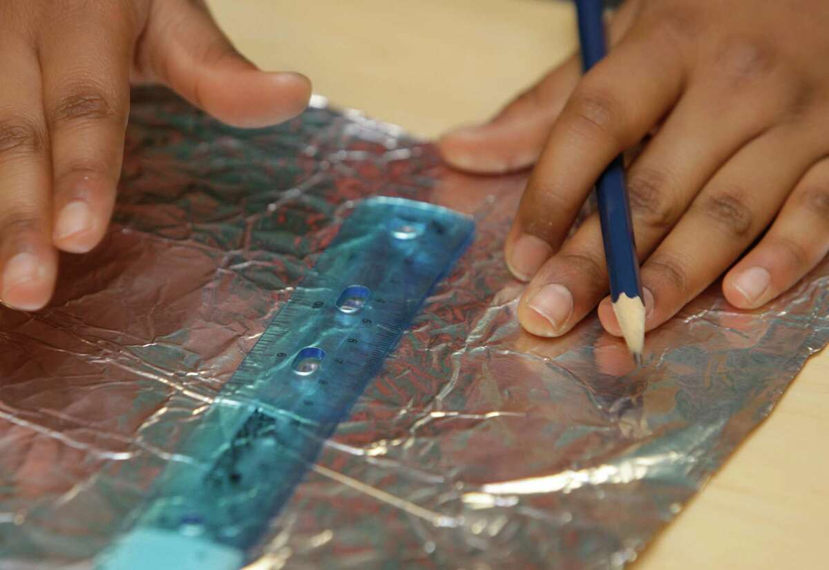 Ramani Talley, 12, right, of team Awesome prepares a foil layer for her team's entry. The students had 20 minutes to use at least 4 different materials such as foil, wax paper, and Styrofoam to make a 14 layer space suit swatch. An impact tester was used to determine the winning design. Fifty area middle-school students participated in the two-week, all-expenses-paid program, founded by former astronaut Dr. Bernard A. Harris Jr..