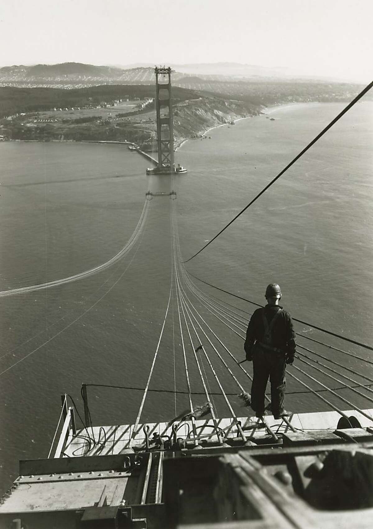1936 - A bridge worker looks across to the San Francisco tower as cables are spun for the Golden Gate Bridge.