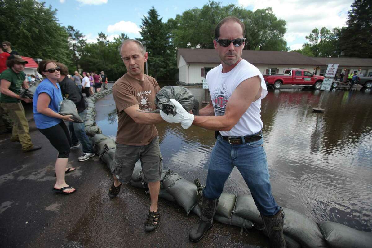 Doug Weisert, center left, of Moose Lake hands Vern Anderson of Moose Lake a sandbag while sandbagging in the parking lot of the Dairy Queen in Moose Lake, Minn., Thursday, June 21, 2012. The waters of the Moose Horn river overflowed in to parts of Moose Lake after record rainfall hit the area. Several homes and business were flooded.