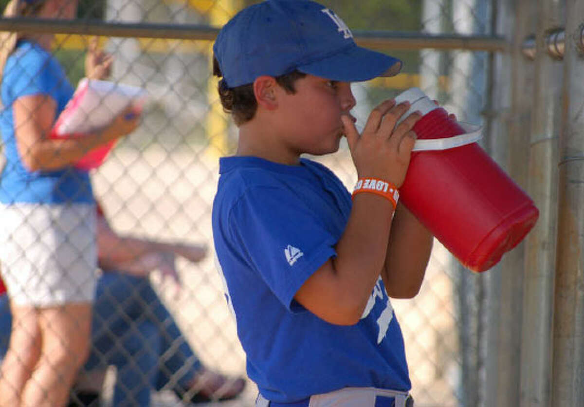 Tim Arguello, 8, takes a break from his first-base duties to stay hydrated during 5:30 p.m. practice at the Mays YMCA on Monday, when the temperature was hovering around 101 degrees. LeAnna Kosub / San Antonio Express-News