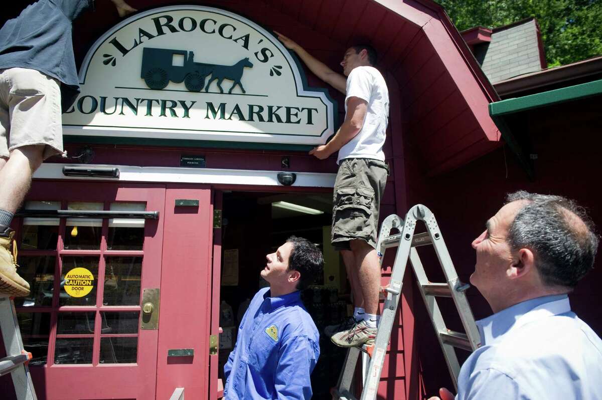 Tommy LaRocca, center, and his father Tommaso LaRocca, right, watch as the new sign is hung at LaRocca's Country Market, previously Giovanni's Country Market, on Old Long Ridge Road in Stamford, Conn., June 27, 2012. The sign, which was hand carved by New England Sign Carvers, is hung by Steve Sutton, left, and Matt Hryniewicz. Tommy LaRocca bought the market from his family two years ago and renovated the space to allow for broader aisles and a 40 foot gourmet counter. The store is now energy efficient and is stocked with more than a third of the products coming from local sources. LaRocca's is holding a grand opening Saturday June 30.