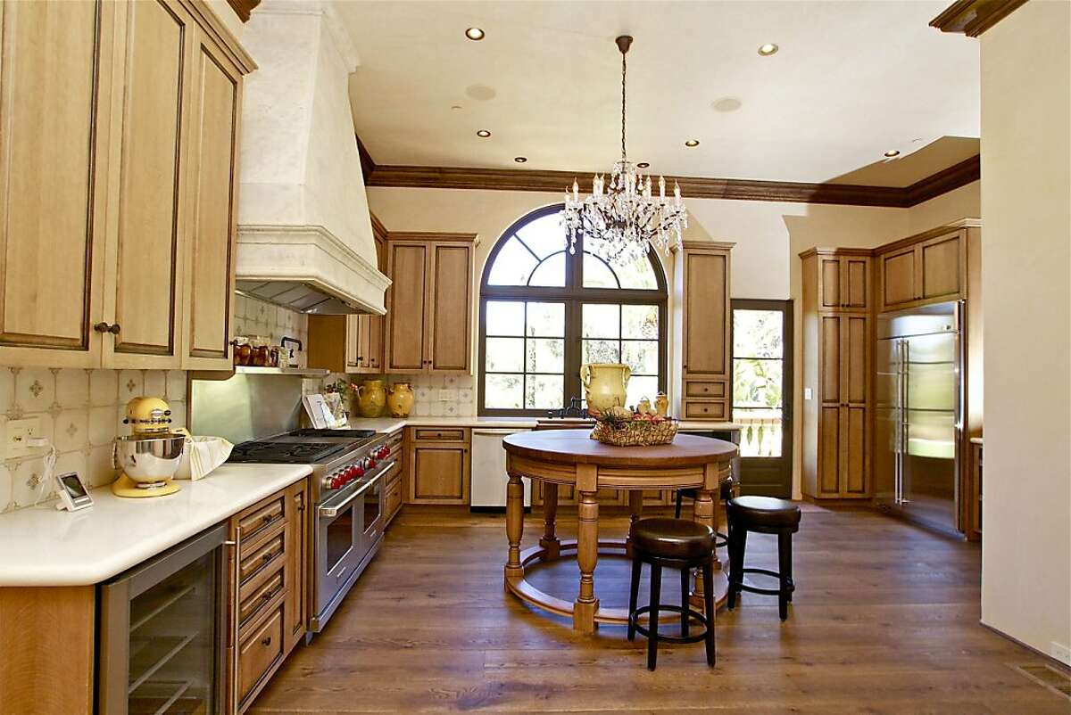 Beneath a decorative chandelier and recssed lighting is a gourmet kitchen, featuring a center island and top-chef appliances, including a hooded six-burner Wolf gas range.