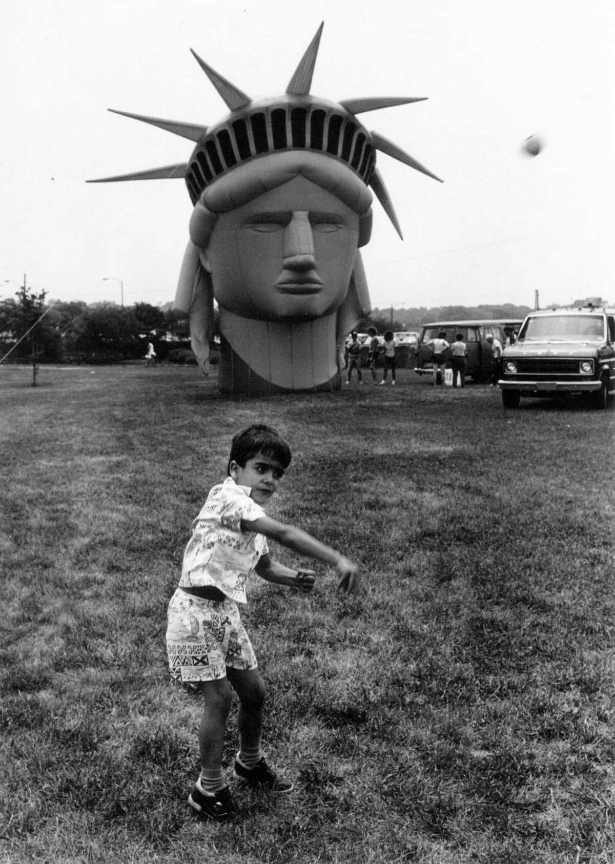 July 4, 1987: Carlos Lopez, 5, of Stamford frolics in Cummings Park in front of a balloon fasimile of the Statue of Liberty's head. The balloon was set to float above the park in the city's fourth of July celebration.