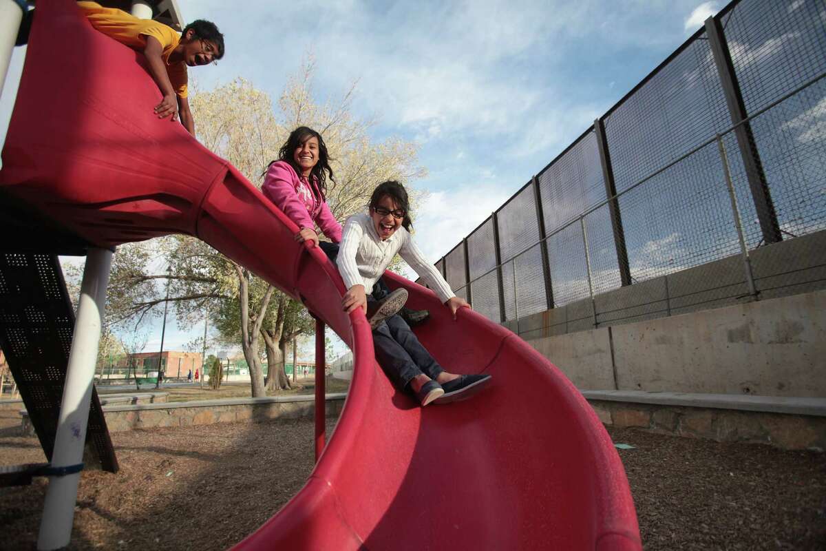 Jonathan Hinojoso, 14, Jessica Guerrero, 15, and Brianna Gonzalez, 9, use the slide in the playground at Chihuahuita Park, which sit against the U.S. Mexico Border fence on Tuesday, March 20, 2012, in El Paso.