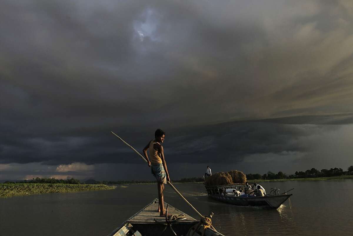 A boat carries flood relief materials as monsoon clouds surrounded the flood affected Gagalmari village in Assam state, India, Monday, July 2, 2012. The floods from monsoon rains in northeastern India killed dozens of people, with more than 2,000 villages inundated as rivers breached their banks, an official said Sunday. (AP Photo/Anupam Nath)