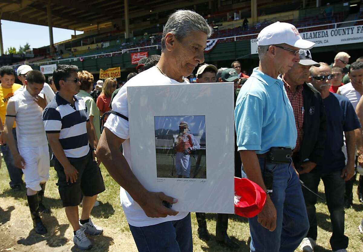 Joe Hernandez carries a portrait of jockey Jorge Herrera after a memorial service for Herrera in the winner's circle at the Alameda County Fair in Pleasanton, Calif. on Friday, July 6, 2012. Hernandez was the valet for Herrera, who died while riding Morito in the eighth race on Thursday.