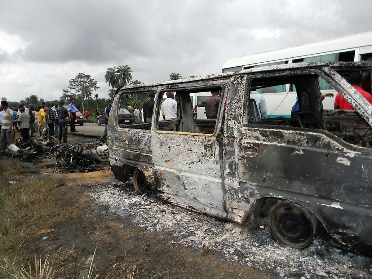 People gather next to a burnt minibus after a Nigerian petrol tanker tipped over and pools of spilled oil caught fire in Okogbe on July 12, 2012. More than 100 people who rushed to scoop up fuel after a Nigerian petrol tanker tipped over on July 12 were killed. Children were among those killed, while dozens more were badly burned, despite a warning from troops who arrived at the crash site that a blaze could ignite at any moment. The tanker driving in the southern Rivers state swerved as it was trying to avoid a collision with three oncoming vehicles including a bus, said Kayode Olagunju, head of the state's Federal Road Safety Commission. AFP PHOTO/STRSTR/AFP/GettyImages