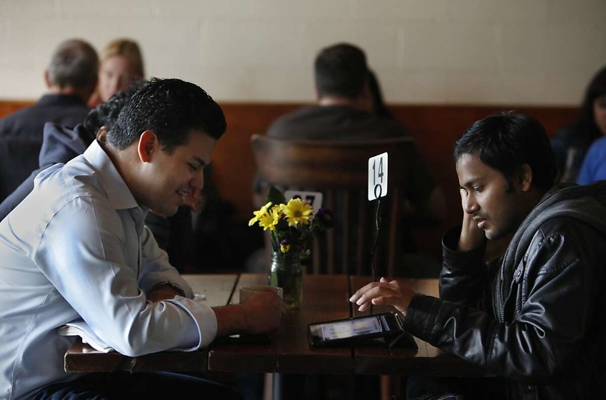 Roberto Santana (l to r), COO of Kloudless, looks at a tablet as Satish Polisetti, co-founder Picatcha scrolls through a display as they discuss work during the lunch hour at The Creamery on Friday, July 13, 2012 in San Francisco, Calif.