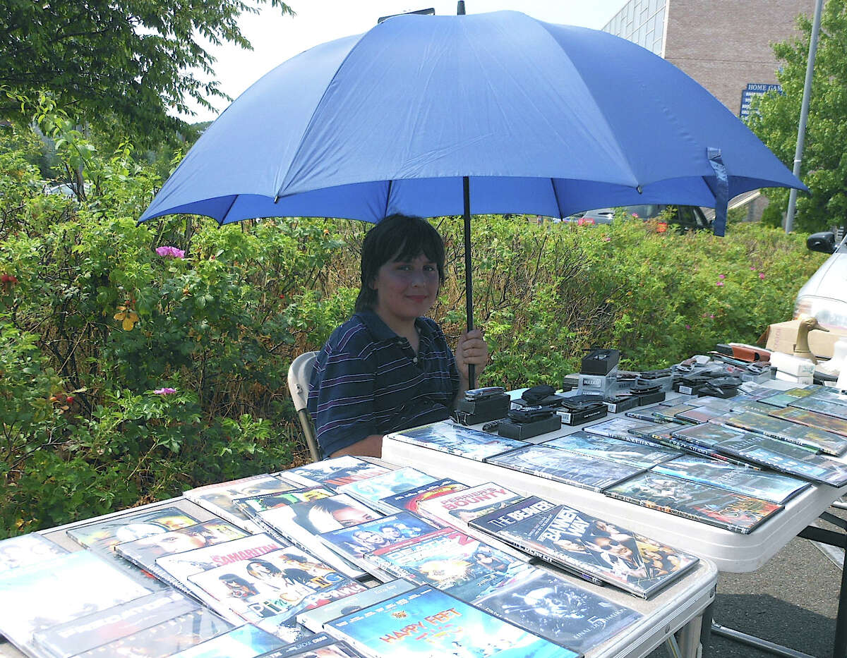 Tyler Gosbin tries to stay cool under a large umbrella while selling DVDs Sunday at Fairfield Ludlowe High School's flea market.