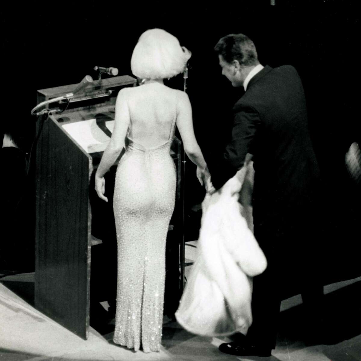 In this May 19, 1962 publicity photo provided by Running Press, Peter Lawford, right, tends to Marilyn Monroe's fur as she prepares to sing "Happy Birthday" to President John F. Kennedy at a Madison Square Garden gala in New York.