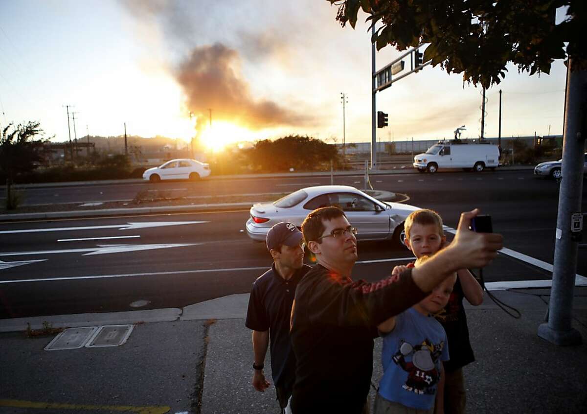 Andres Locky takes a photo of himself in front of plumes of smoke emanating from the Chevron oil refinery on Monday, August 6, 2012 in Richmond, Calif.