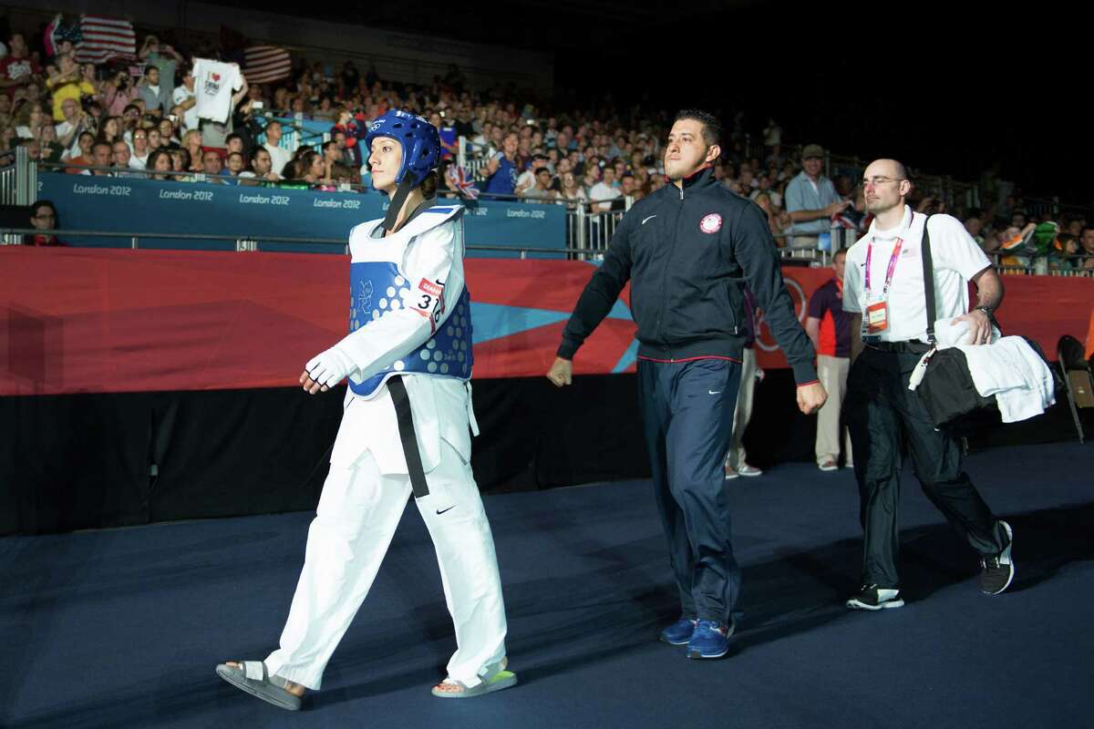 Diana Lopez of the USA, left, is cheered by supporters as she enters the arena with her coach, and brother, Jean Lopez, center, to fight Hou Yuzhuo of China during a women's -57kg preliminary round taekwondo bout at the 2012 London Olympics on Thursday, Aug. 9, 2012. Lopez lost to the two-time world champion 1-0 in sudden death.