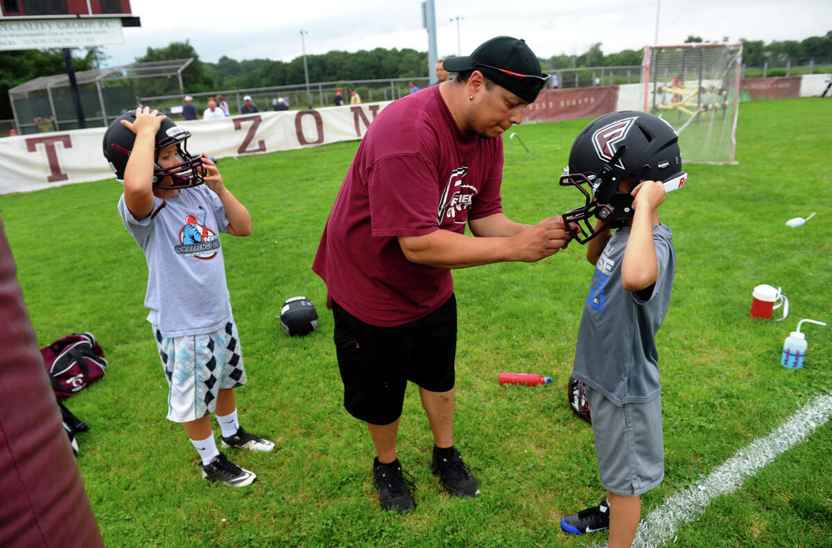 Fairfield Giants assistant coach Johnny Vasquez, center, helps adjust his son Jayson's helmet, during youth football pratice at their field on Old Dam Road in Fairfield, Conn. on Wednesday August 1, 2012.
