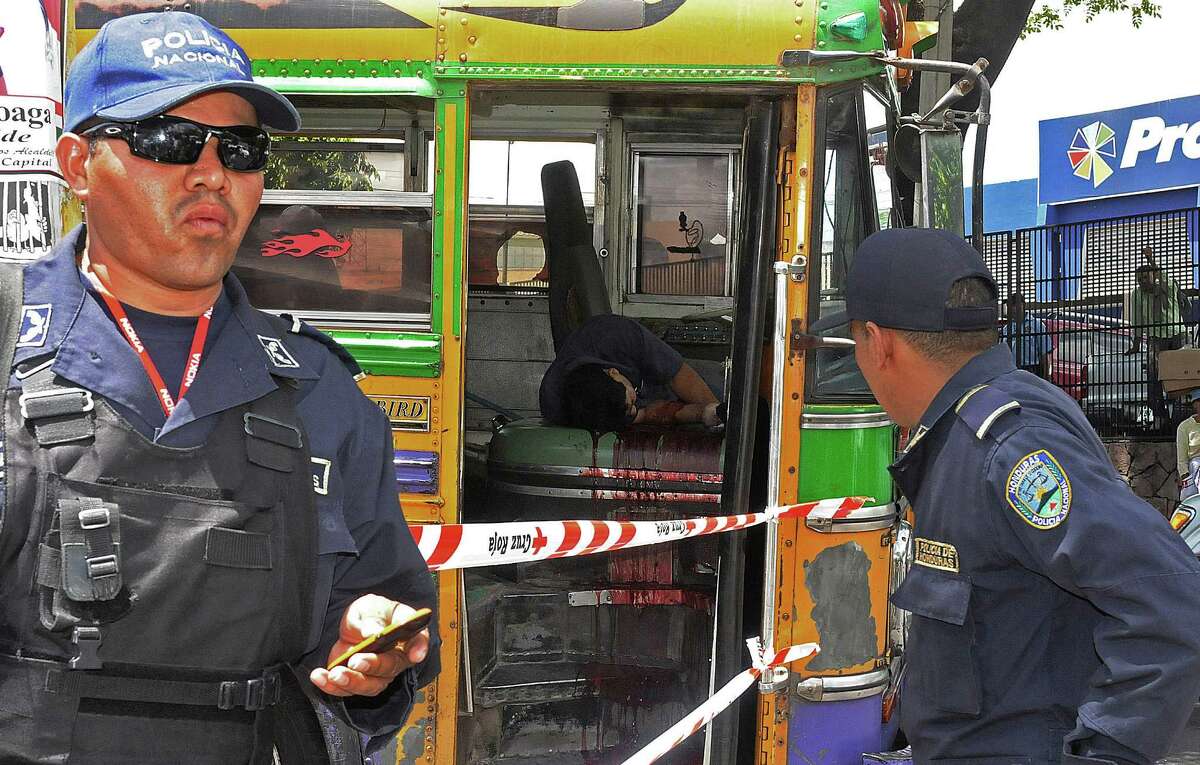 In this Aug. 6, 2012 photo, national police stand at a crime scene where a public bus driver was slain by an unidentified attacker in Tegucigalpa, Honduras. According to police on the scene, the driver was a probable victim of gang extortion, which is common throughout Central America. In Honduras, taxi drivers and business owners are also used to extortion, but the practice now has reached into the one place many people considered their last remaining safe haven: their home. (AP Photo/Fernando Antonio)