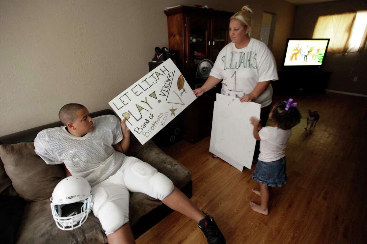 Cindy Earnheart, right, shows a sign she made for her son twelve-year-old Elijah Earnheart, left, as her three year old daughter Larnai tugs at their home in Mesquite, Texas, Thursday, Aug. 16, 2012. The 6-foot, 300-pound 12-year-old has been ruled ineligible to play Pee Wee football in the Dallas area. Despite being a young seventh-grader, officials say is more than twice the maximum allowable Pee Wee weight of 135 pounds. (AP Photo/LM Otero)