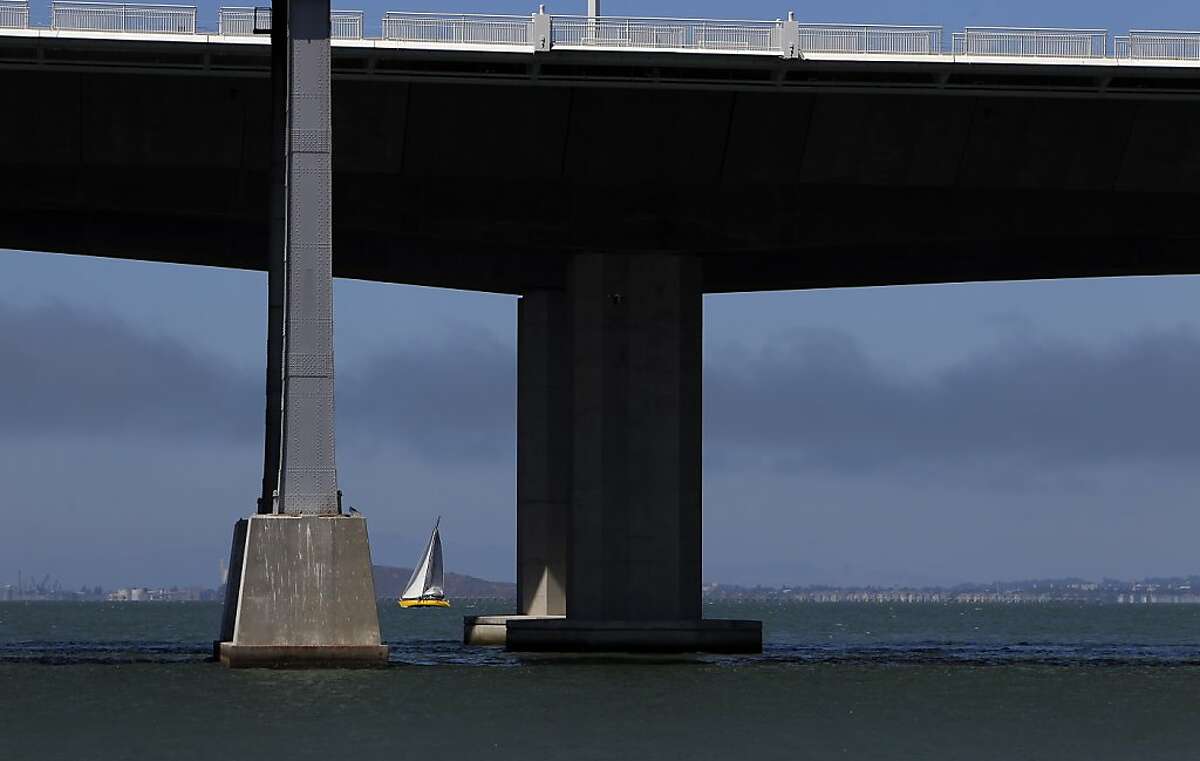 A sailboat is seen between the supports of the new and old eastern span of the Bay Bridge on Thursday, August 16, 2012, in San Francisco, Calif., as crews begin tensioning the new suspension cables. Caltrans is asking water vessels to avoid going under the new span as crews will now be working on the exterior of span, potentially creating a hazard for craft going underneath. Crews on the new east span of the Bay Bridge are preparing to start "transfering the load" or lifting the suspension section of the new bridge onto the suspension cables and off of the temporary trestles that have supported it during construction.