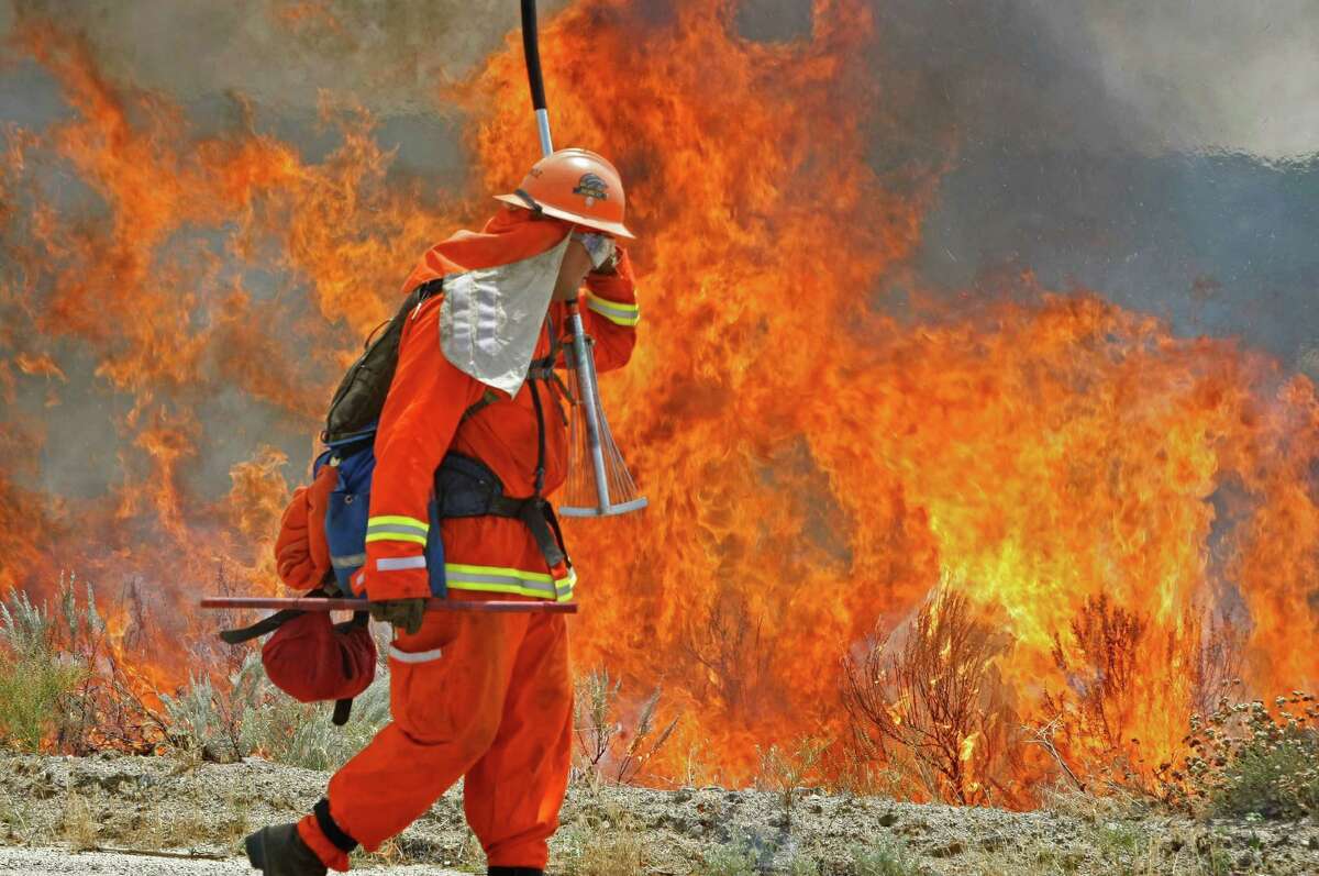A firefighter from the Norco Conservation Camp shields his face against the heat of a backfire his crew intentionally set along Montezuma Valley road in Ranchita, Calif. on Thursday.