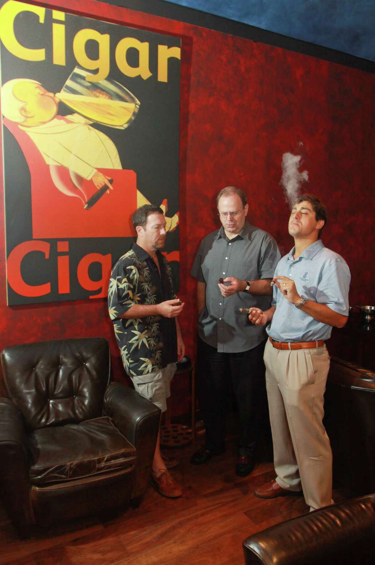 (For the Chronicle/Gary Fountain, August 24, 2012) Owner Rich Tisch, from left, general manager Tom Parks and Matias Adrogue, a trial lawyer for Cigar Cigar, enjoy cigars in the private lounge at Cigar Cigar in Sugar Land Town Square. They are not able to smoke a cigar or pipe on their outdoor patio due to a Sugar Land Town Square ban.