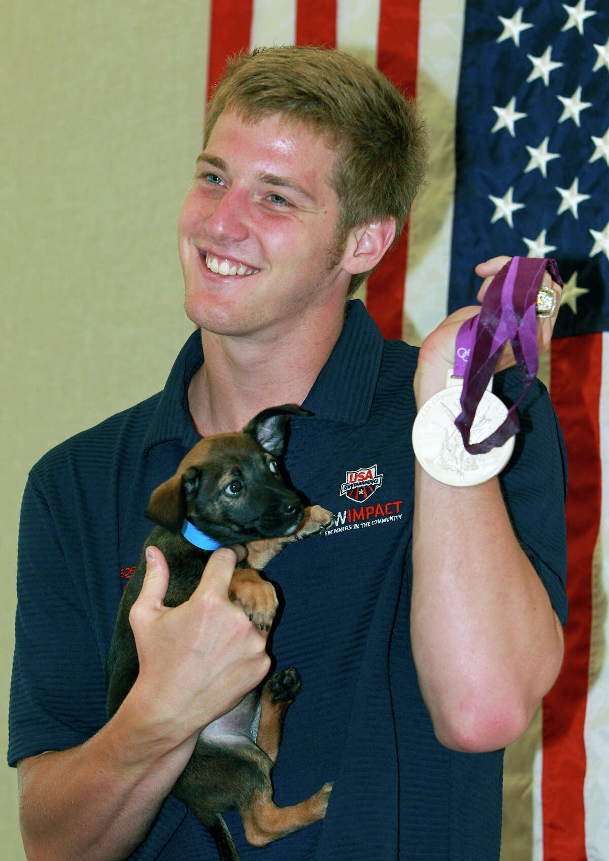 Jimmy Feigen holds a puppy, Cargill, and his silver medal as he meets with fans at the San Antonio Humane Society on August 30, 2012.