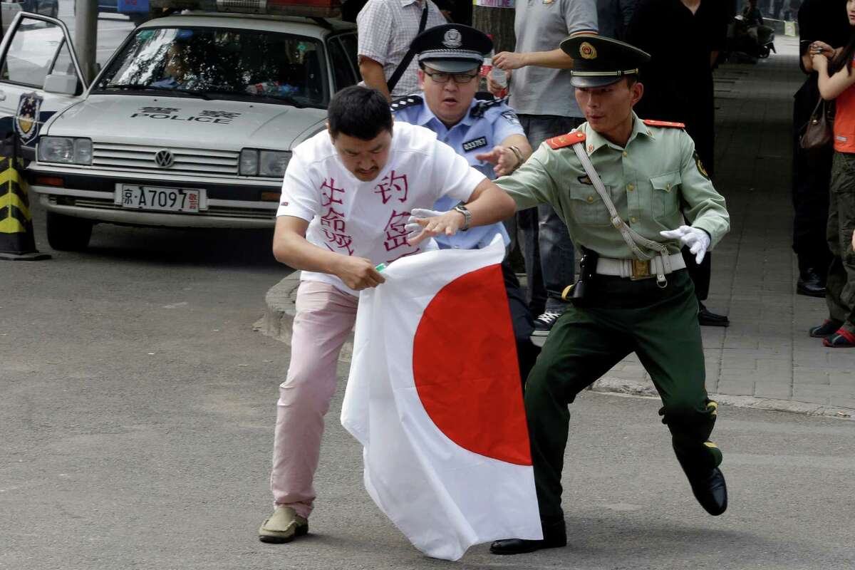 Two security officers try to stop a Chinese man as he attempts to burn a Japanese flag on Tuesday outside Japan's embassy in Beijing. Japan's announcement Monday that it intends to buy two disputed islands has sparked anger in China.