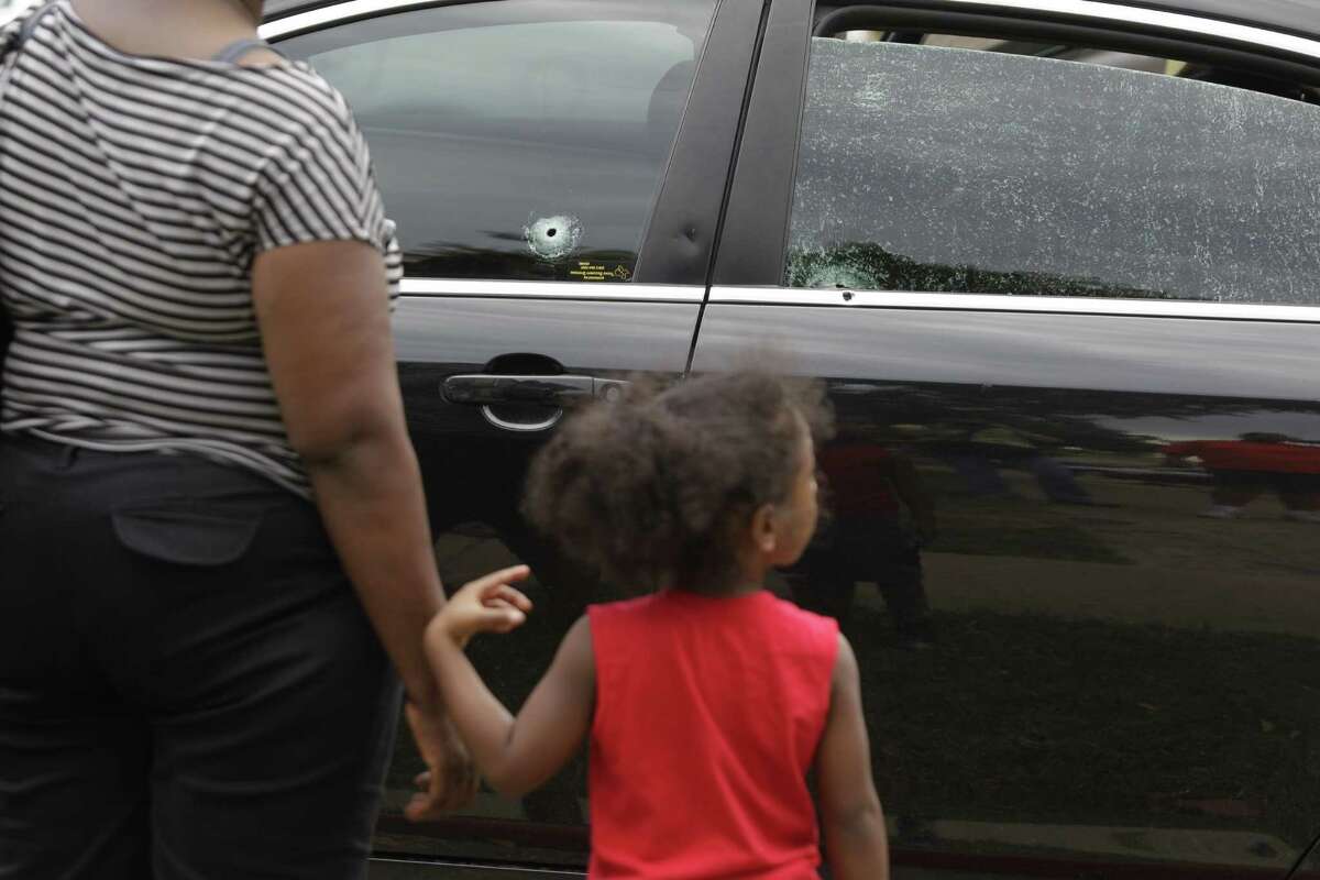 People look at bullet holes Wednesday in one of the cars involved in a shooting at the apartment complex The Mint at Dairy Ashford, near Westbranch.