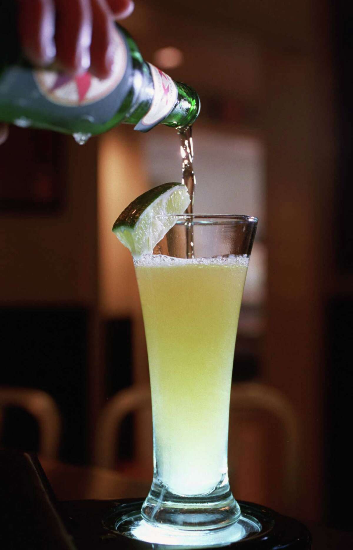 Dos Equis beer is added to a glass containing tequila and lime juice.