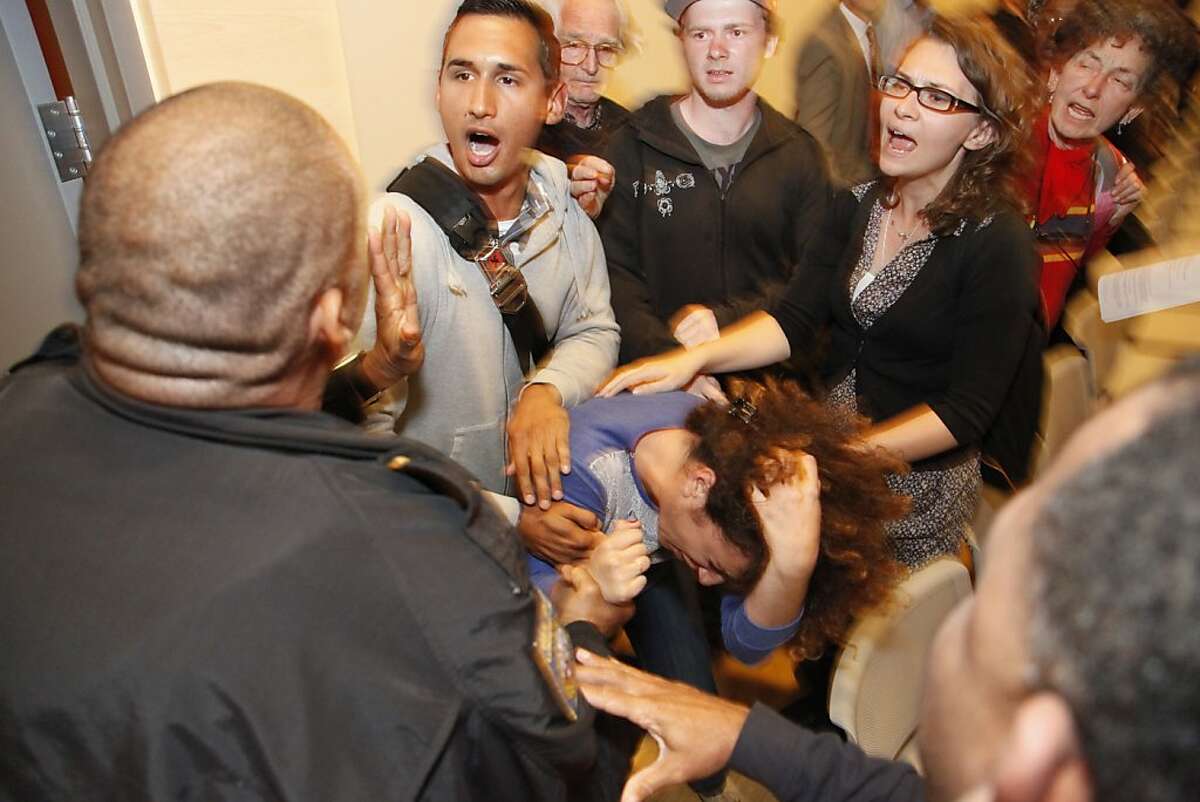 Lalo Gonzalez tries to protect Ali Oligny from being dragged out of the CCSF Board of Trustees meeting by police on Tuesday, Sept. 11, 2012 at the City College of San Francisco's chinatown campus. The board of trustees is leaning towards asking the state for a special trustee to help them preserve their accreditation which many they loudly opposed. Gonzalez is a graduate of San Francisco State University and Oligny is currently UC Berkeley student.