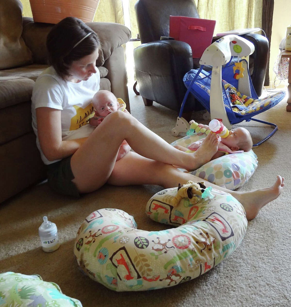 Lauren Perkins feeds Levi on her lap while balancing a bottle with her foot for Caroline.