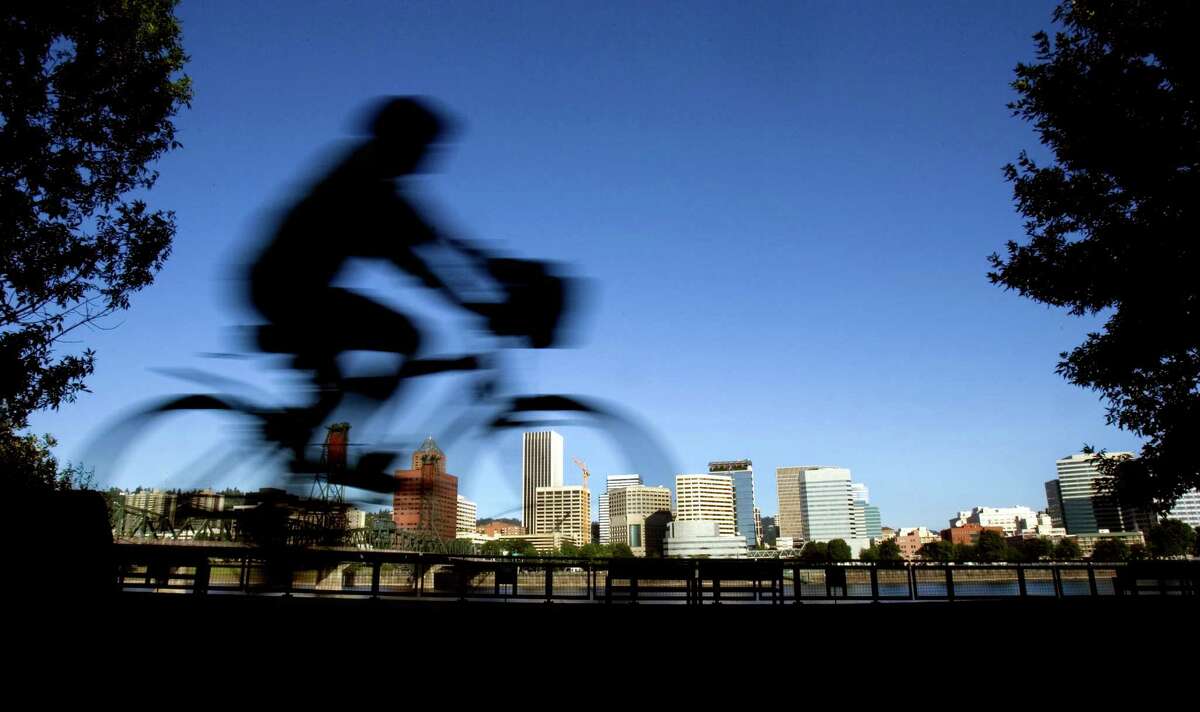 FILE - In this July 10, 2008 file photo, a bicyclist is a blur traveling along the east bank of the Willamette River as the downtown skyline is bathed in early morning sunlight in Portland, Ore. A famous quip by Fred Armisen on the television show "Portlandia" led Portland State University researchers to investigate the reality behind the comment. The quirky IFC network series pokes fun at the Oregon city's many eccentricities. (AP Photo/Don Ryan, File)