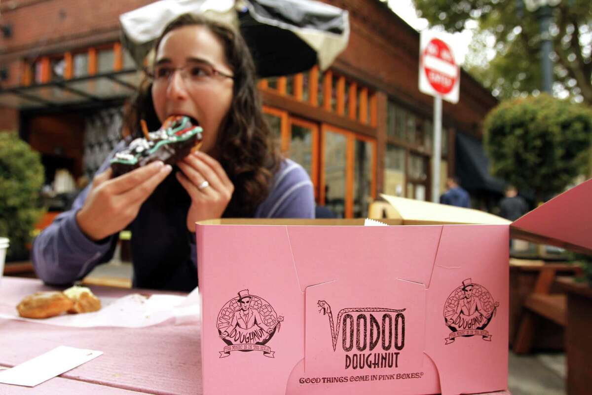Jennie Myren, who is from Iowa and spending her honeymoon in Portland, enjoys the signature doughnut shaped like a voodoo doll with a pretzel stick stake through its' heart outside the famous Voodoo Doughnuts shop in downtown Portland, Ore., Wednesday, Sept. 19, 2012. Researchers at Portland State University found that the Portland atmosphere and culture is a magnet for the young and college educated, even though a disproportionate share of them are working in part-time jobs or positions that don?t require a college degree. (AP Photo/Don Ryan)