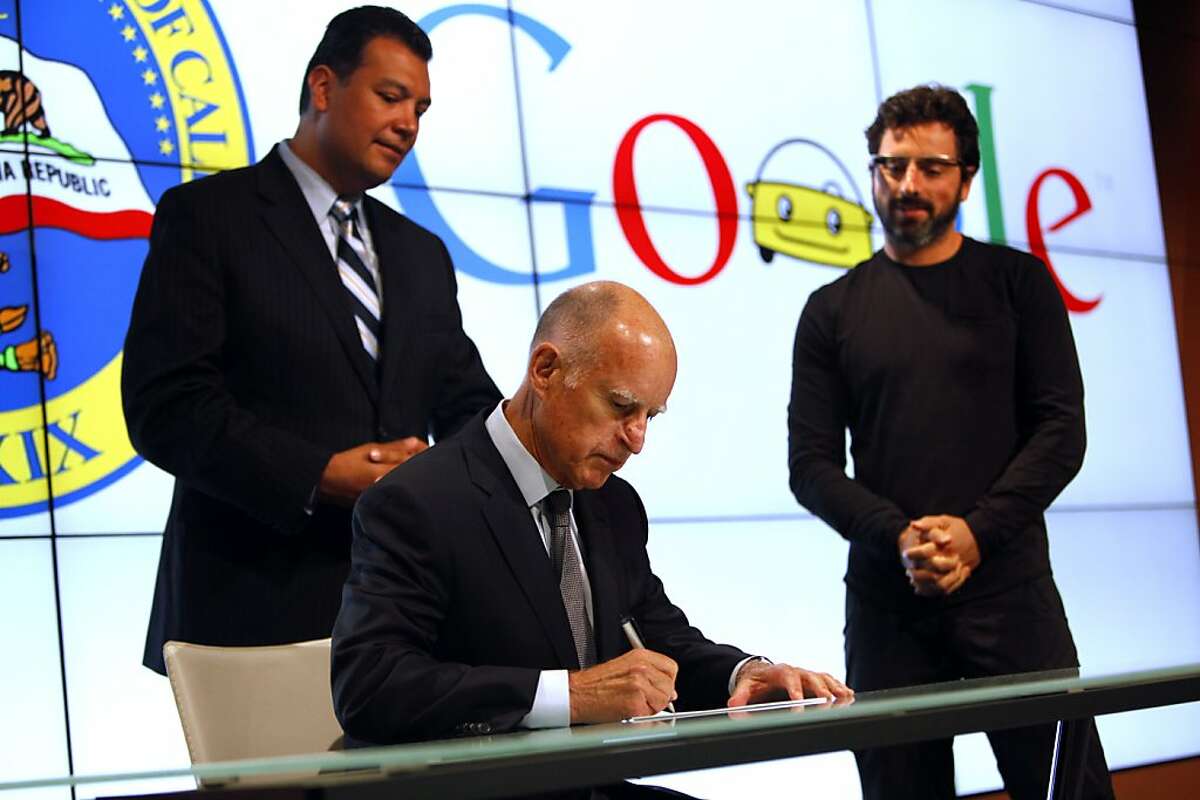 Gov. Jerry Brown signs a new bill regulating the ability of still-experimental driverless vehicles to operate on California roads at Google headquarters in Mountain View, Calif., Tuesday, September 25, 2012, as Senator Alex Padilla, left, and Google co-founder Sergey Brin, right, look on.