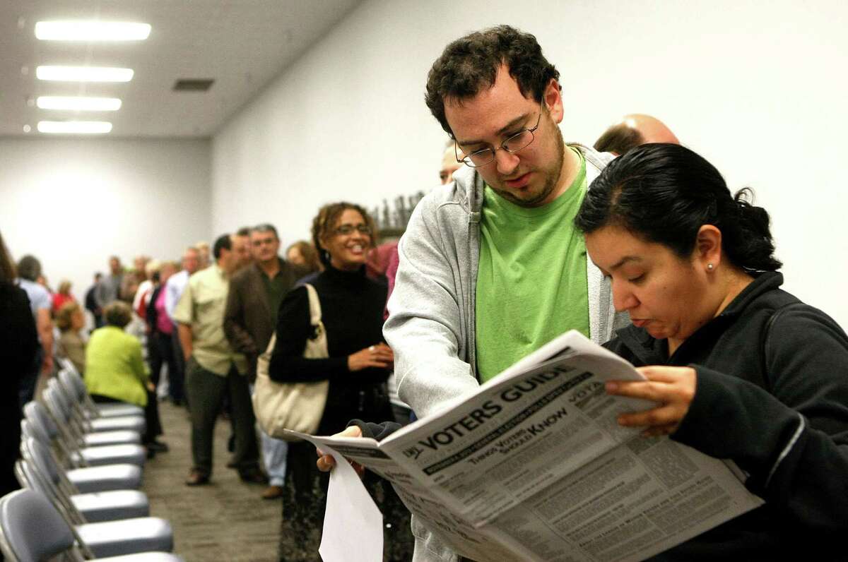 David Zaga and Monica Ortega read a Voters Guide while waiting in line with several others Friday during early voting at the Harris County Precinct 3 Trini Mendenhall Sosa Community Center.
