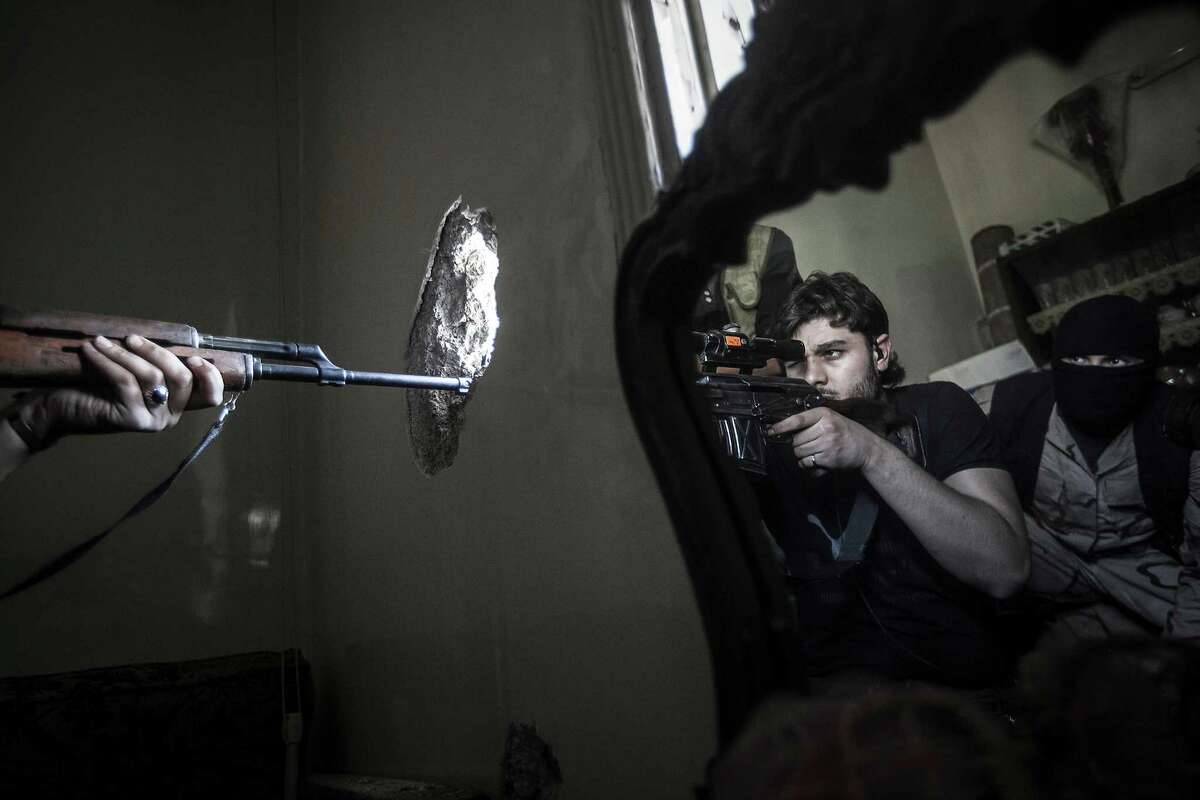 A rebel sniper aims as another rebel fighter is reflected in a mirror in Aleppo, Syria. Airstrikes and shells from tanks killed at least 23 people Tuesday.